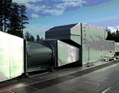 Large gray industrial fans on rooftop, surrounded by trees and sky.