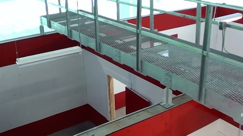 Metal walkway crosses indoor space with open doors and red-white walls.