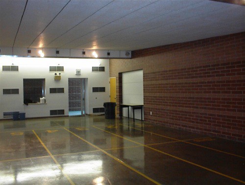 An empty room with brick walls and a shiny floor. A doorway and tables are against the walls.