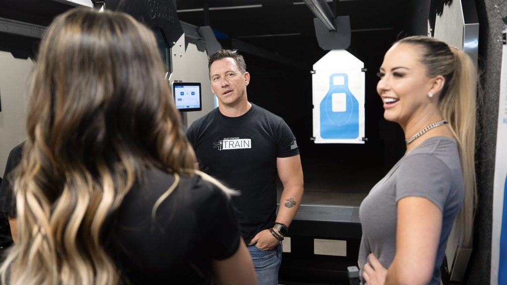 A group of people talk inside a shooting range, with a paper target visible in the background.