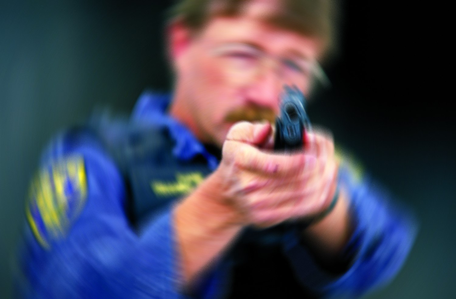 Blurry image of a man in uniform aiming a handgun.