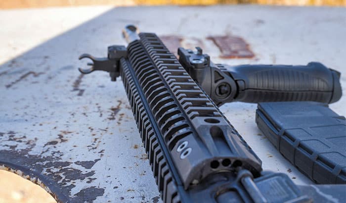 Close-up view of a black tactical rifle with attached grip and magazine resting on a table.