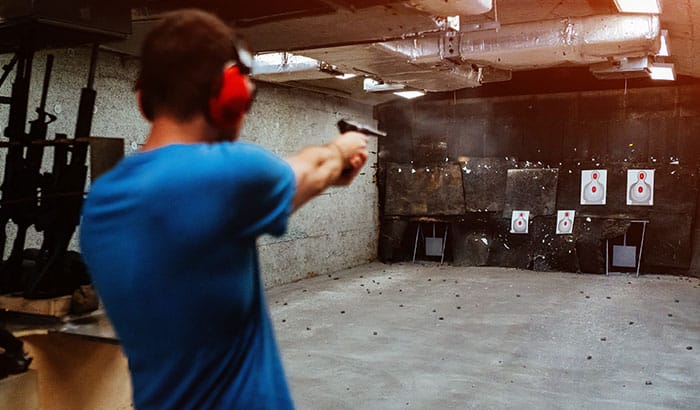 Person shooting a handgun at targets in an indoor shooting range, wearing red ear protection.