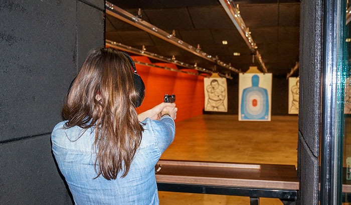 Person aiming a handgun at a target in an indoor shooting range, wearing ear protection.