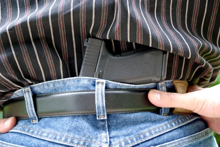 Close-up of a concealed handgun tucked into the waistband of jeans under a striped shirt, showing concealed carry position.
