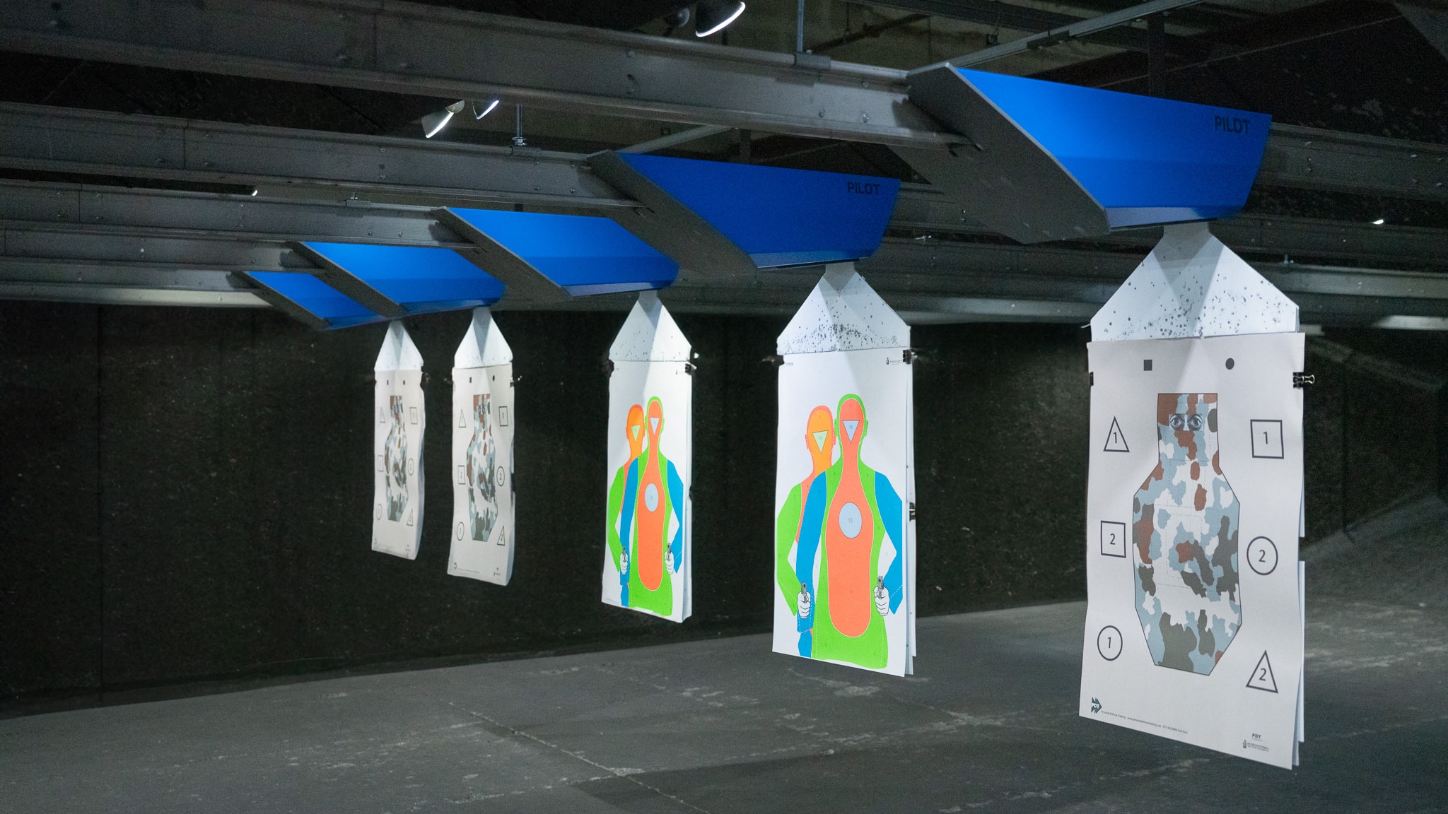 Target sheets hang under blue supports in an indoor shooting range.