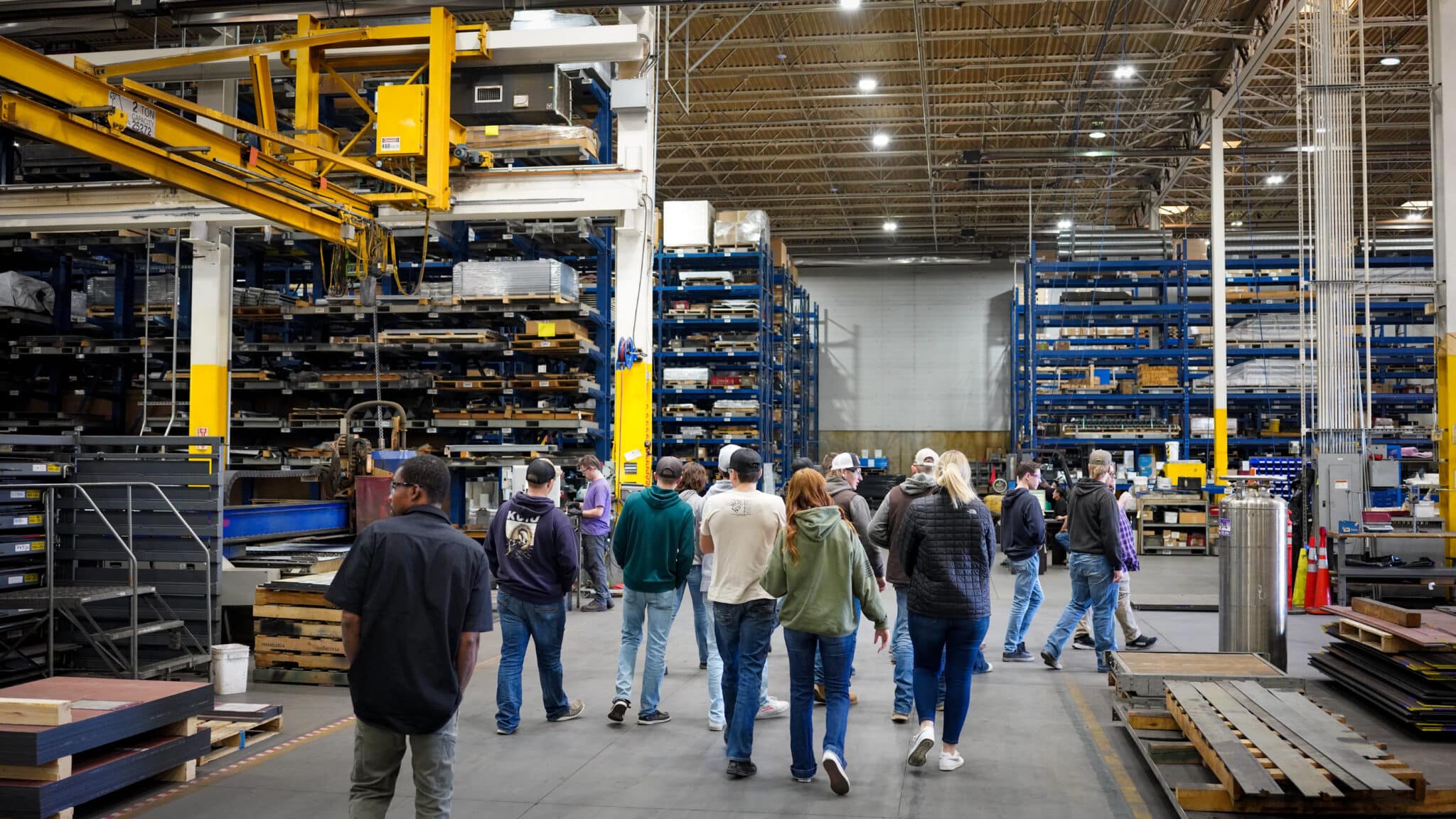 Group walking in a spacious warehouse with shelves and equipment around them.