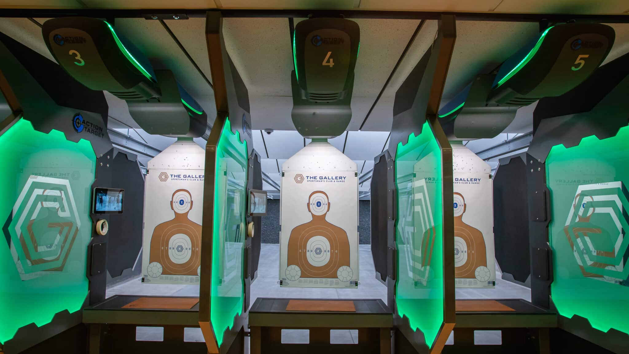 Indoor shooting lanes with glowing green stalls and human silhouette targets.