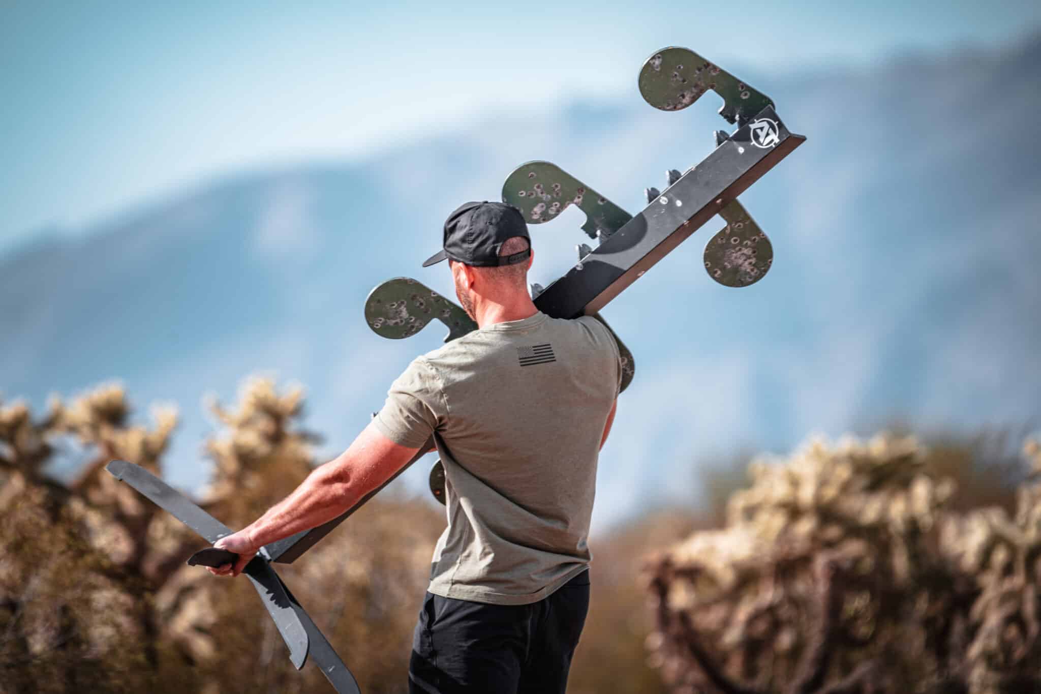 Person carrying a steel target rack across an outdoor range.