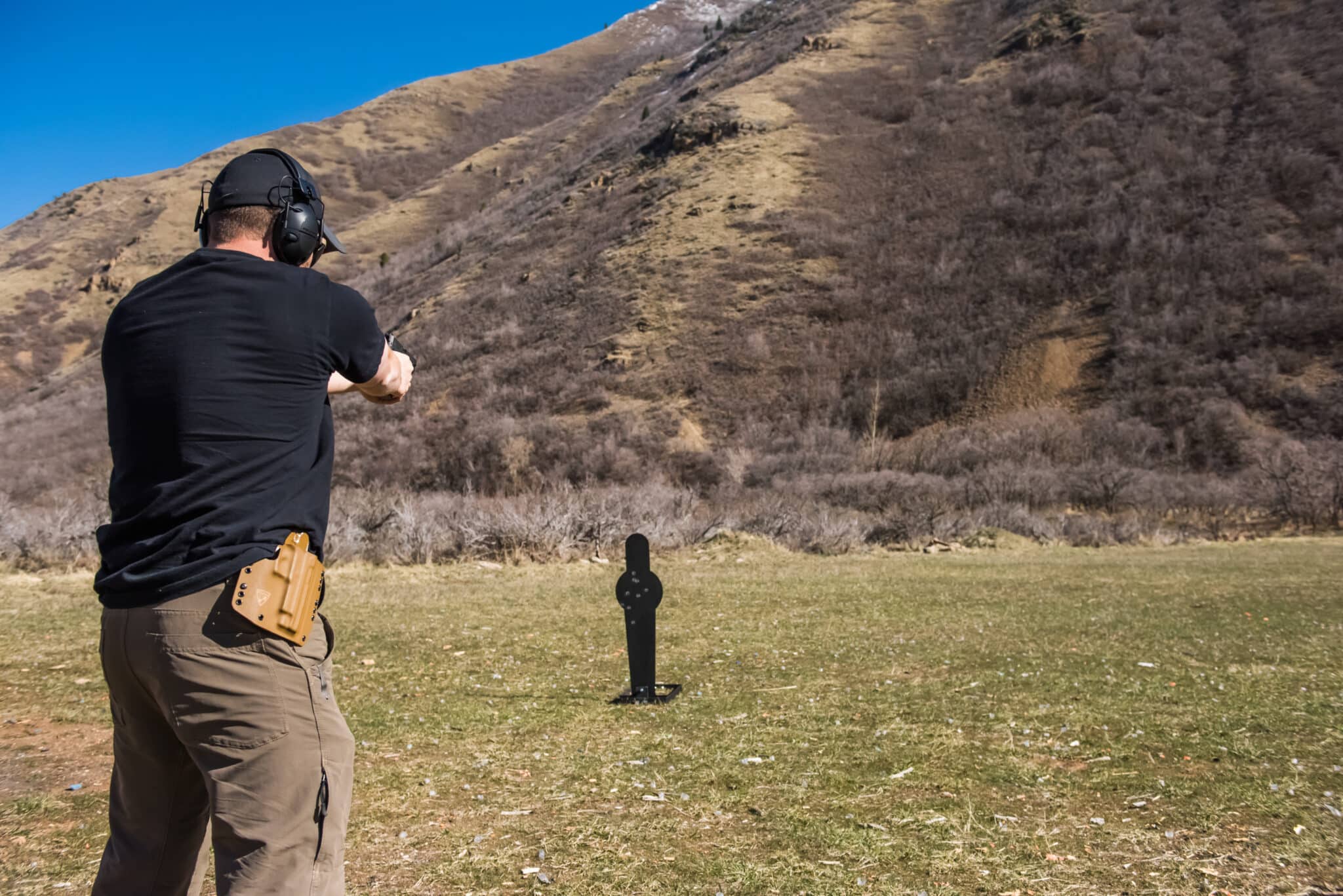 Shooter aiming at a steel target on an outdoor range with mountains in the background.