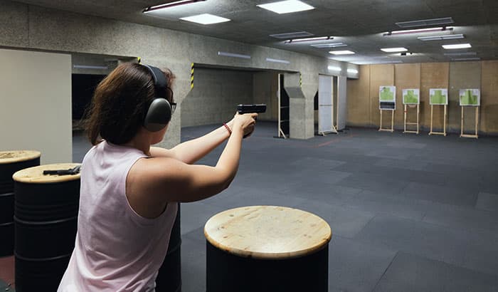 Person wearing ear protection aims handgun at targets in an indoor shooting range.
