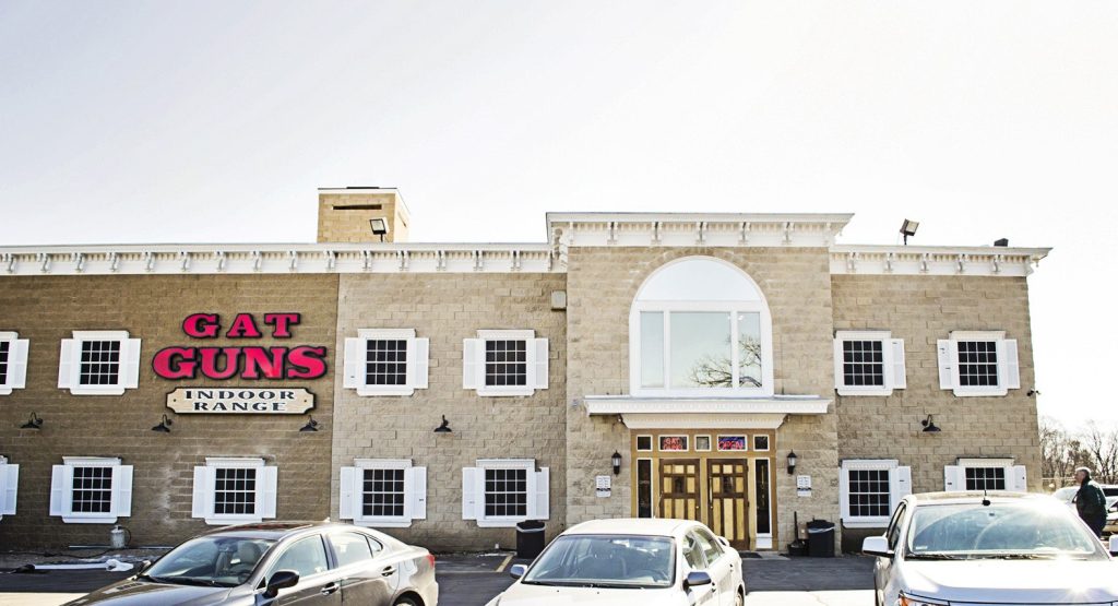 Building facade with sign "GAT GUNS INDOOR RANGE"; cars parked in front.