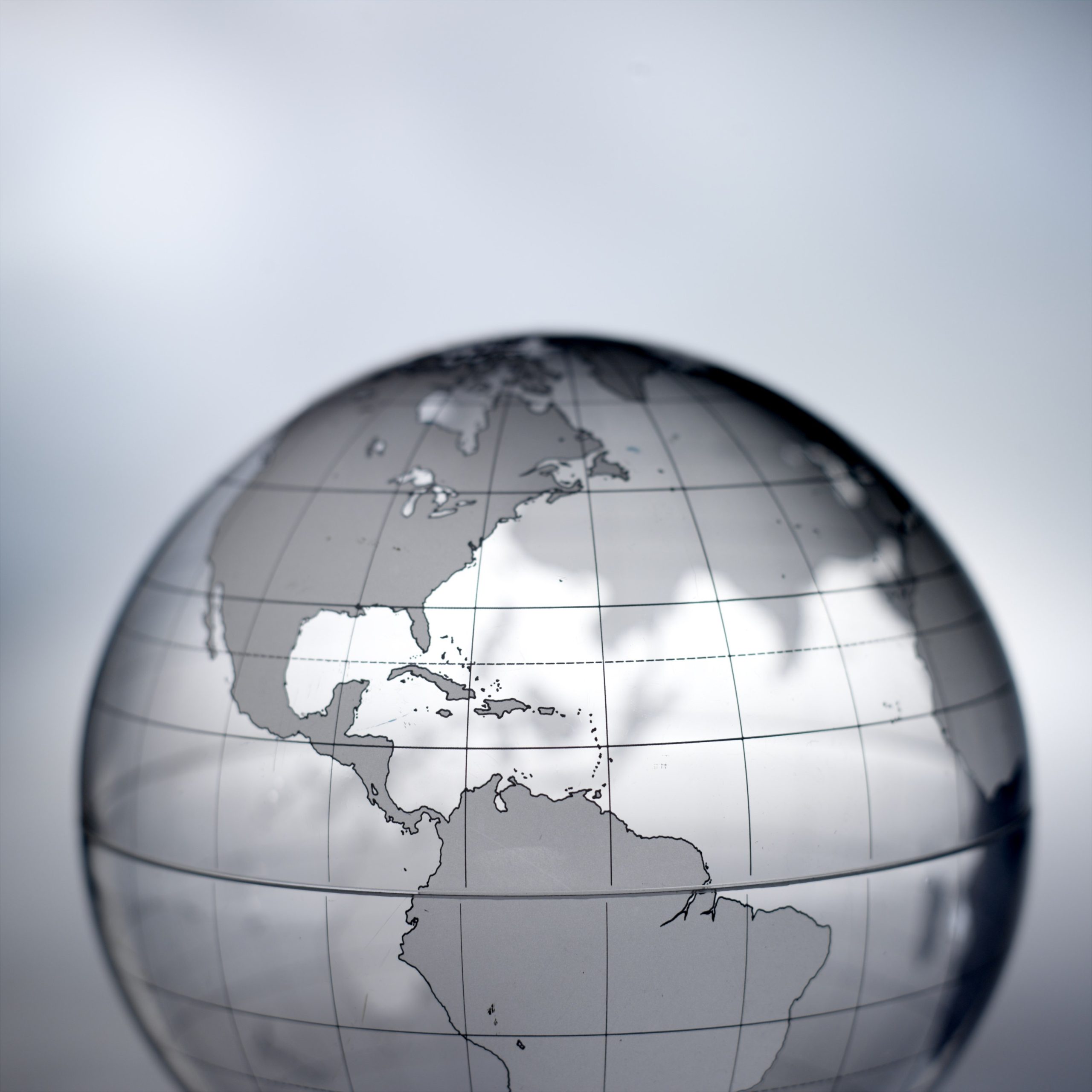 Transparent glass globe showing North and South America with etched latitude and longitude lines against a soft gray background.