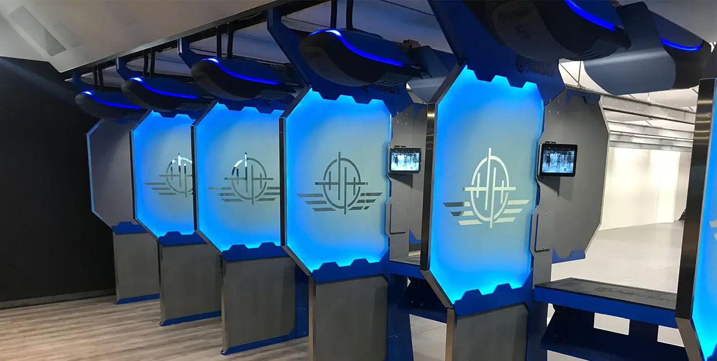 Modern indoor shooting range lanes with illuminated blue partitions, digital control screens, and overhead target retrieval systems.