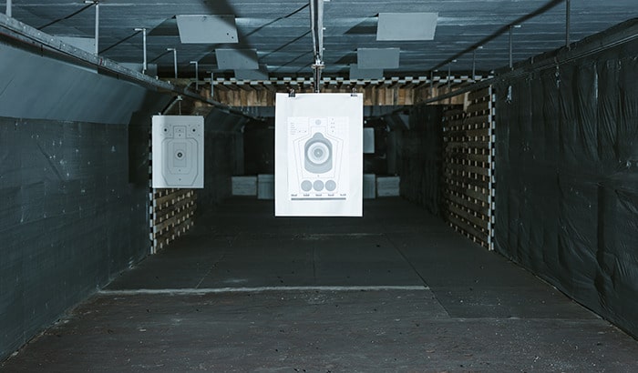 Indoor shooting range with paper bullseye targets suspended from target retrieval system above firing lanes.