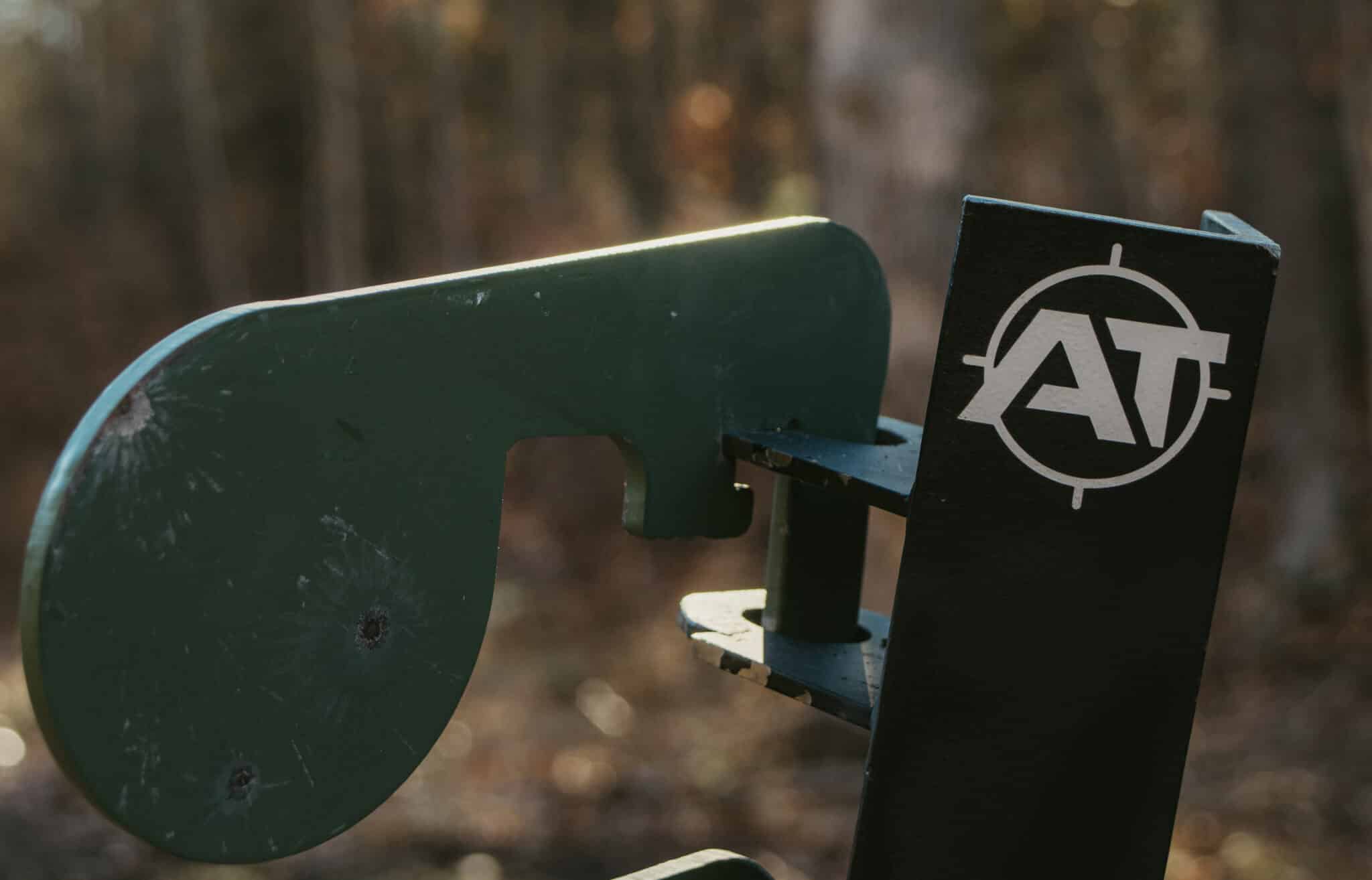 Metal shooting target with "AT" logo; forest background.