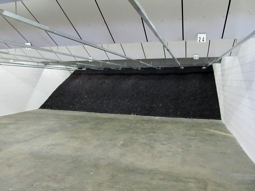 Indoor shooting range with a bullet trap at the back wall, concrete floor, and overhead target tracks.