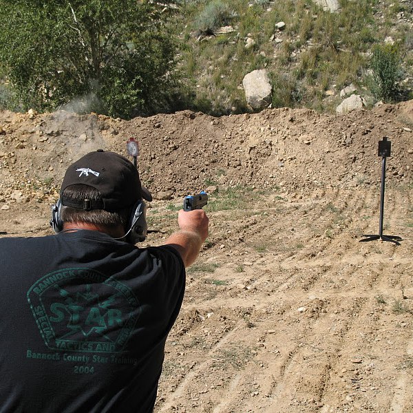 Man aiming handgun at a steel target on an outdoor shooting range.