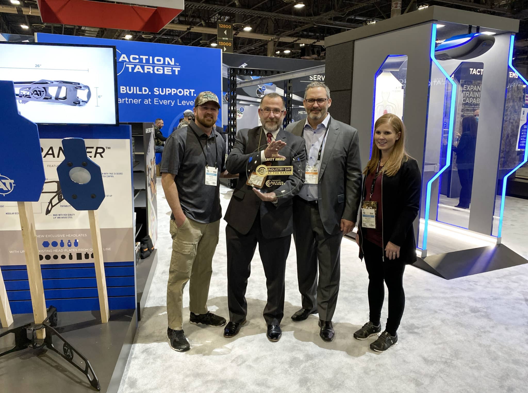 Four people smile holding an award at an event booth. Text: "Action Target. Build. Support. Partner at Every Level."