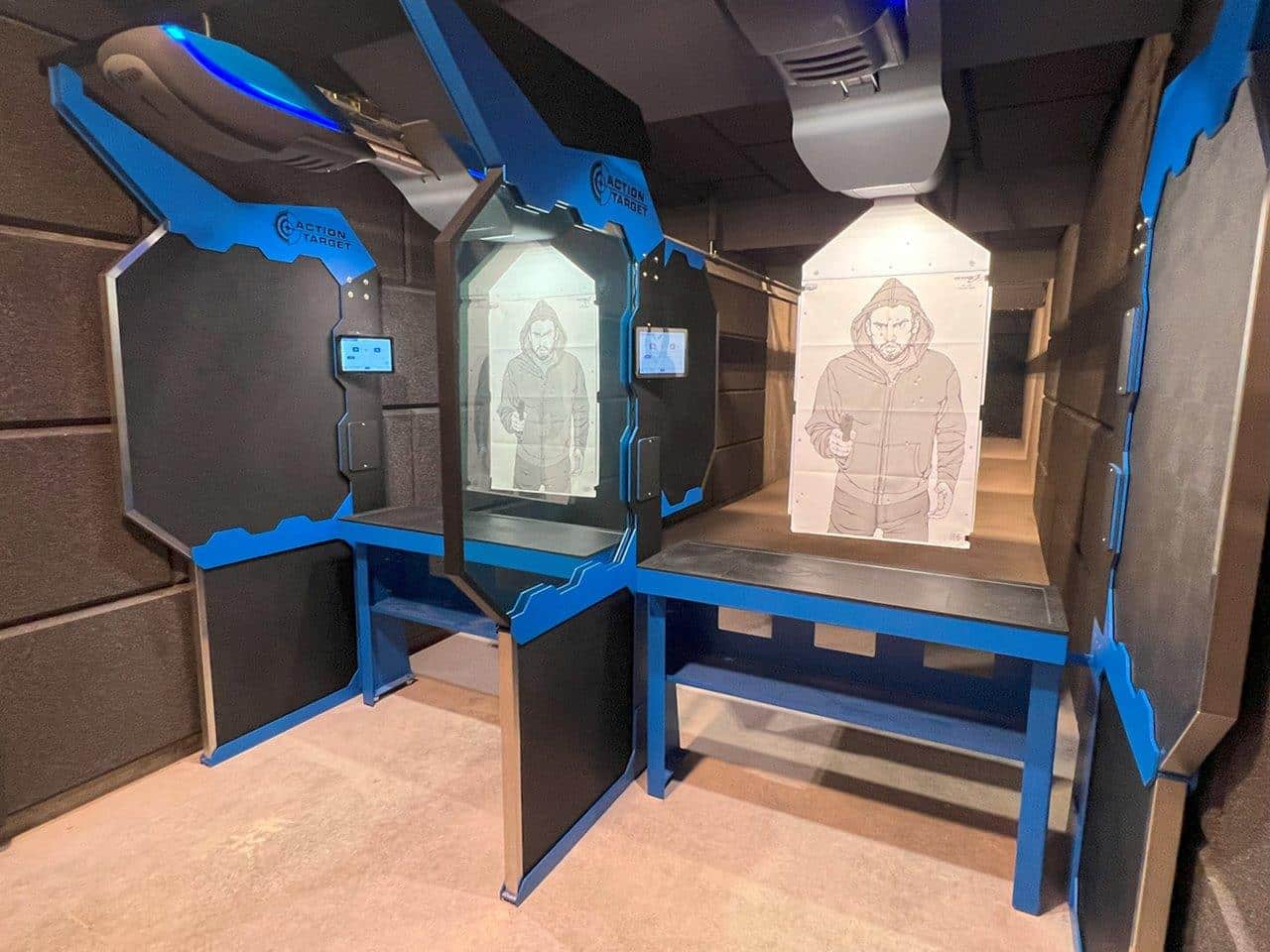 Shooting range lanes with targets, featuring a figure in a hoodie, in an indoor facility.