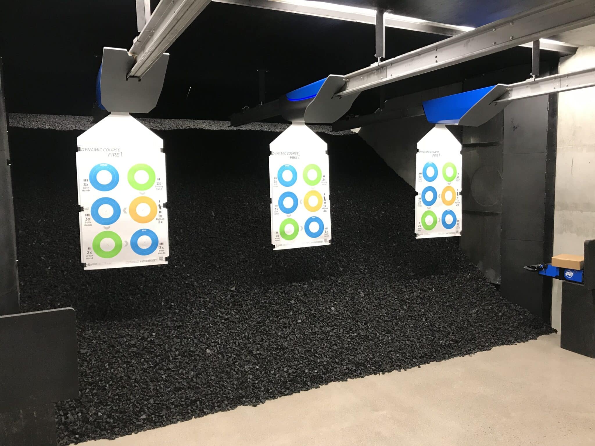 Indoor shooting range with three bright training targets hanging in front of a trap backstop designed for bullet containment.