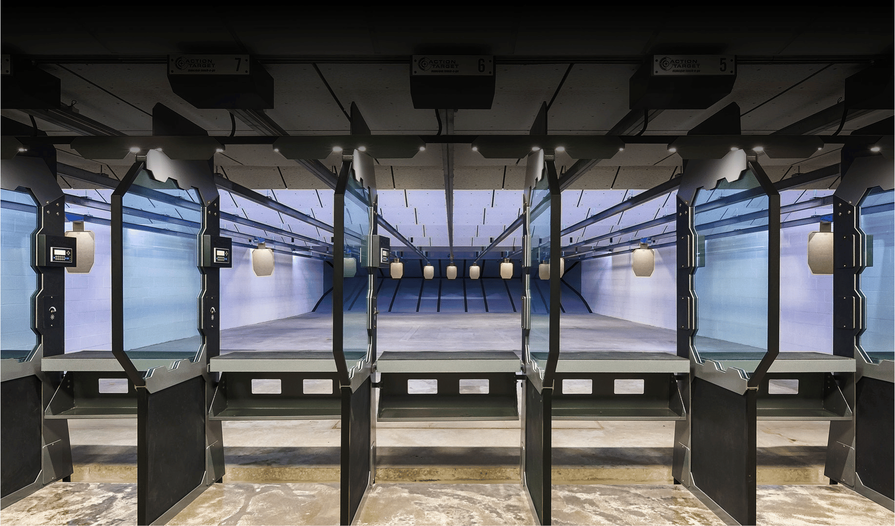 Shooting range booths, empty, lined up indoors with targets in the distance.