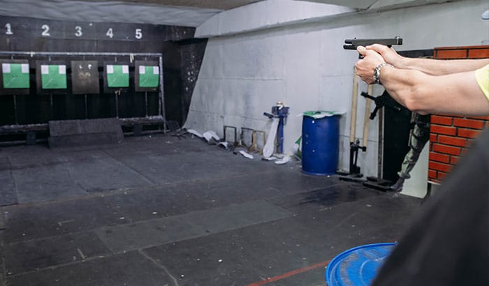 Hands aiming a pistol at targets in a shooting range with numbered lanes and safety gear.