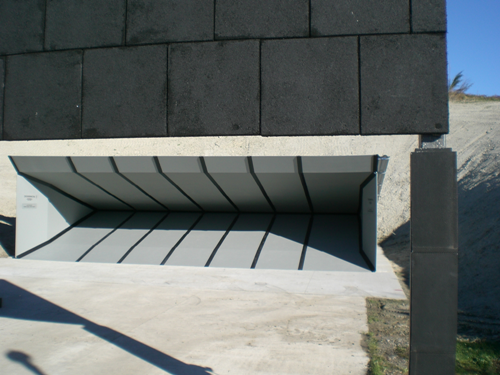 Outdoor shooting range bullet trap with angled steel panels and overhead canopy designed to capture and contain fired rounds.