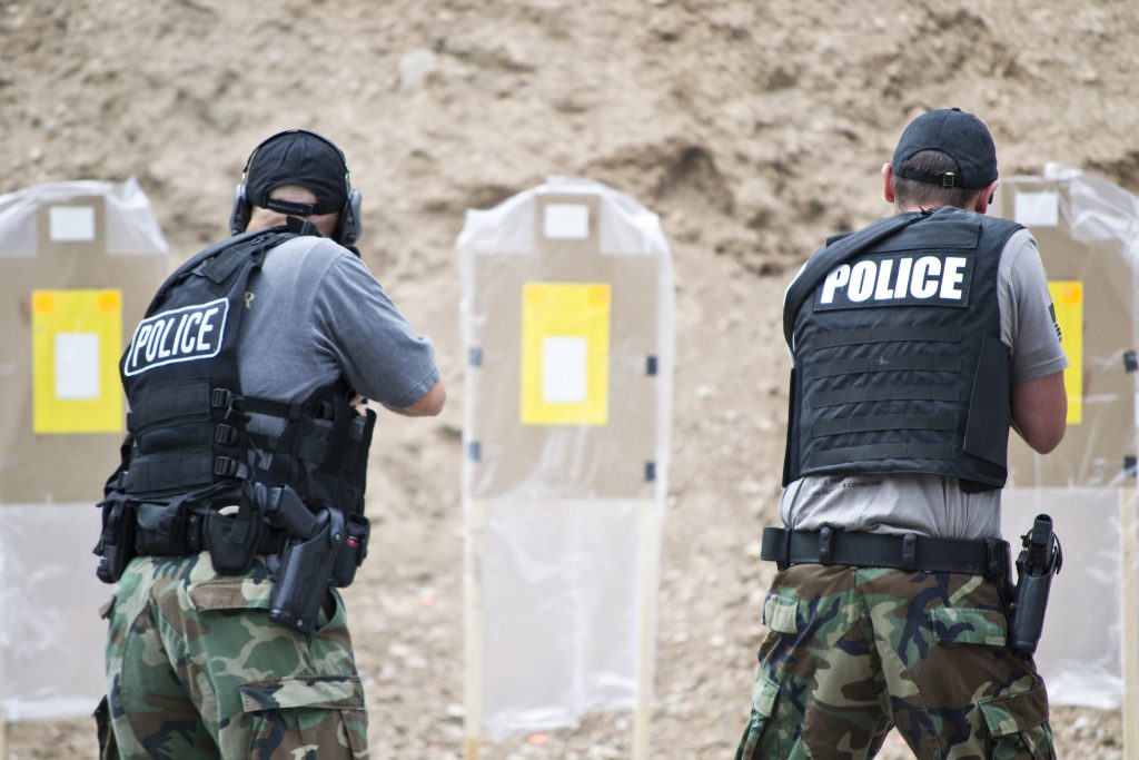 Officers aiming at targets on a shooting range; wearing tactical vests, labeled "POLICE."