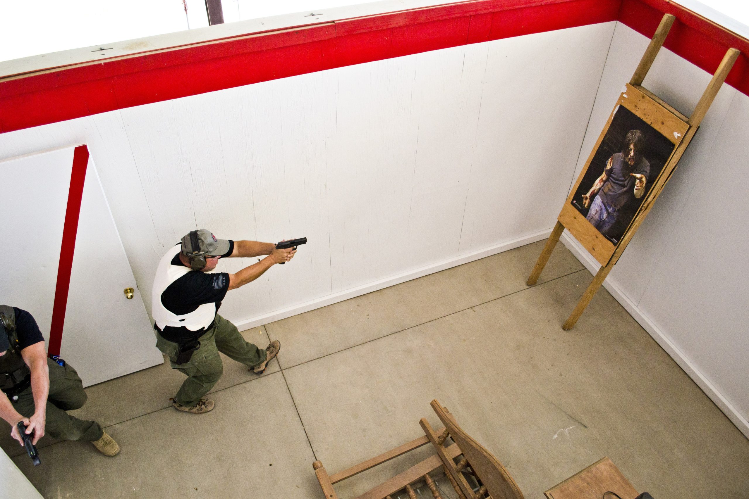 Two men in tactical gear aiming handguns during a live action training drill inside a shoot house.