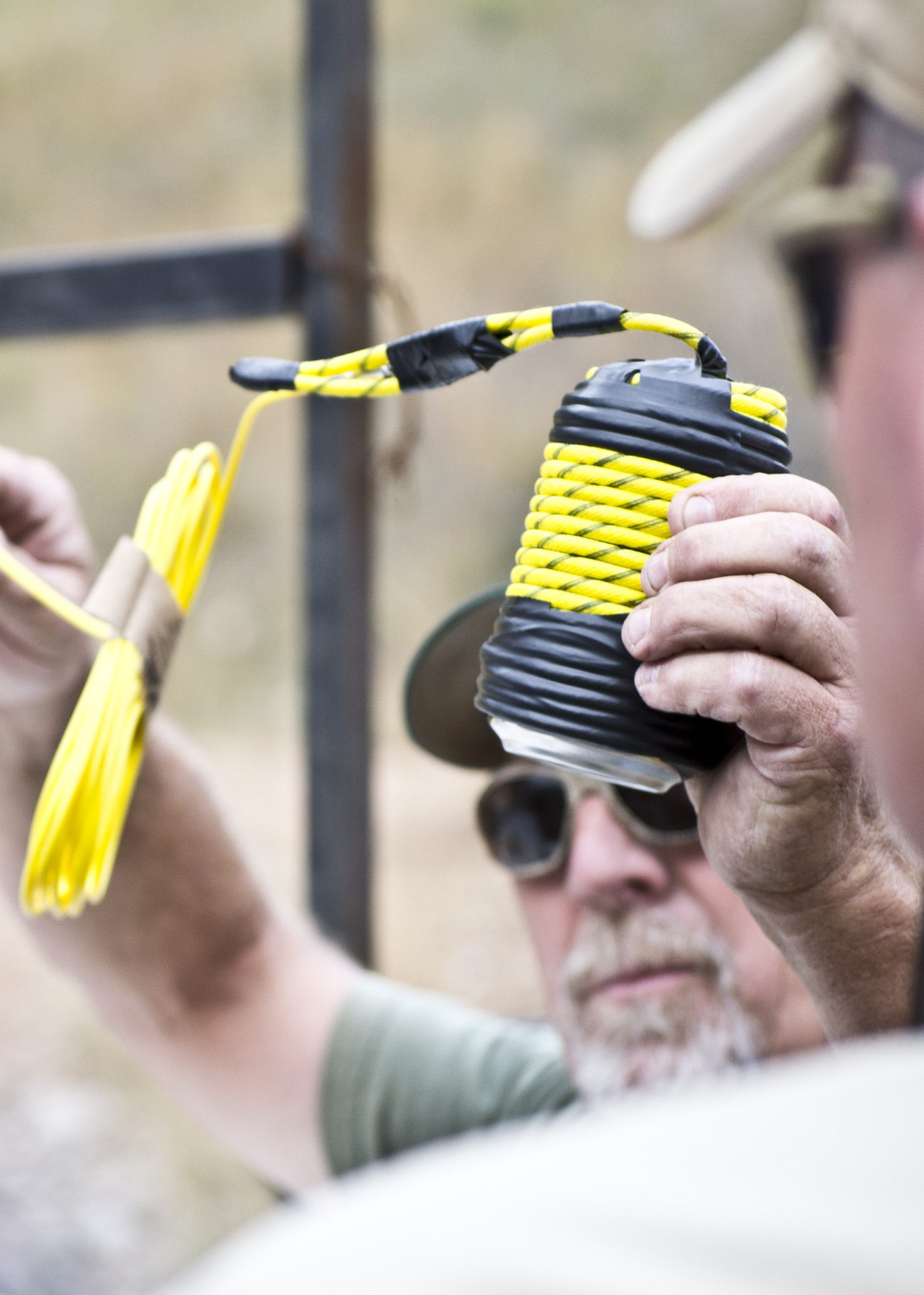 Man holding a yellow rope tightly wrapped with black tape during an outdoor training or setup activity.