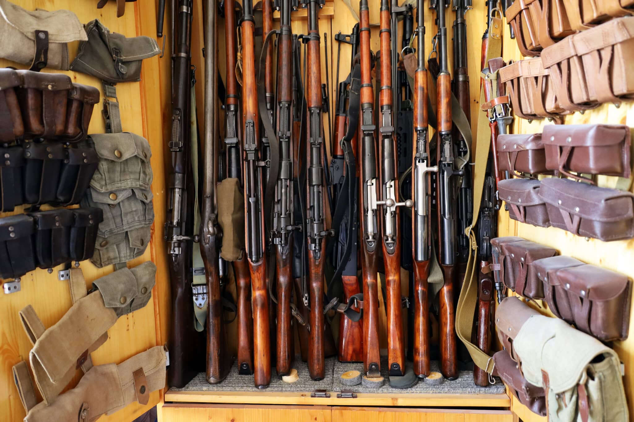 Collection of rifles and ammunition pouches stored in a wooden cabinet.