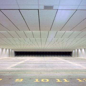 Empty indoor shooting range with numbered lanes, bright lighting, and protective ceiling panels.