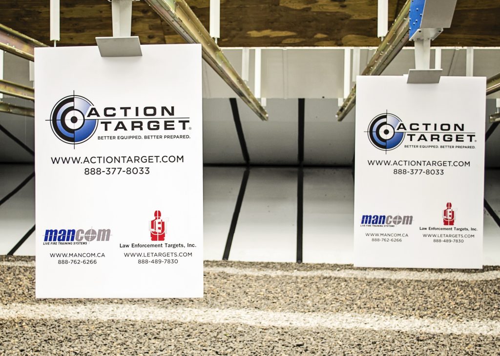 Indoor shooting range with Action Target advertisement boards displaying company logo, website, and contact details.