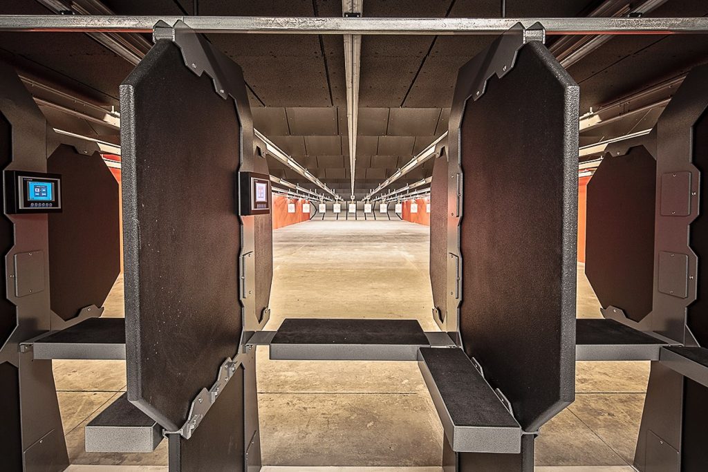 Firing range booths with electronic control panels facing targets down the lit shooting lanes.
