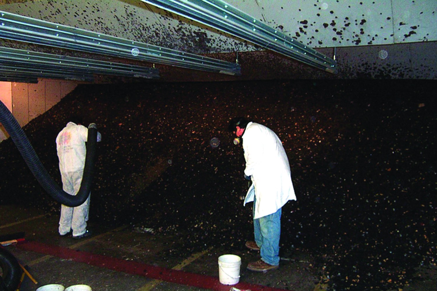 Workers in protective suits and masks cleaning lead and bullet debris from an indoor shooting range bullet trap area.