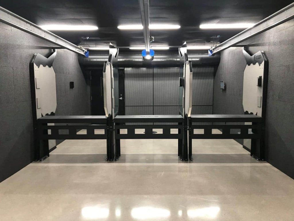 Empty shooting range with three lanes, barriers, and overhead lights in an enclosed space.