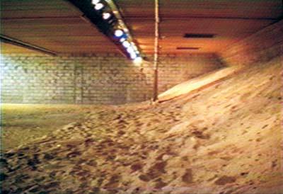 Sand dune indoors under ceiling lights, next to brick wall.