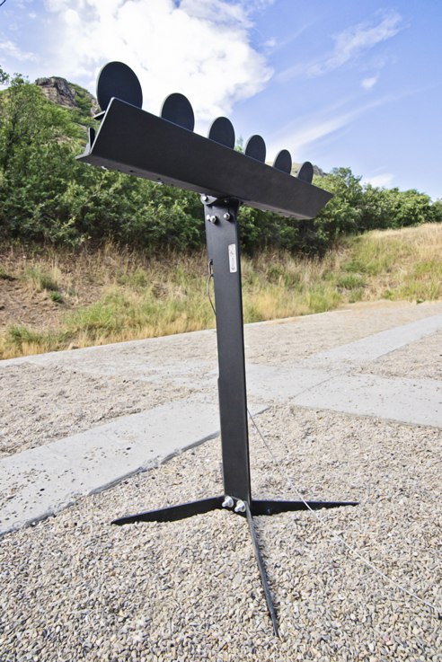 Metal target stand with circular plates, outdoors on gravel with trees in the background.