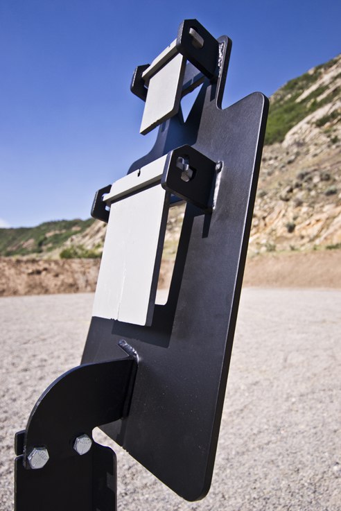 Metal target stand with plates; set outdoors on gravel with mountains in background.