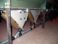 Metal chutes funnel materials into pipes, part of an industrial processing setup.