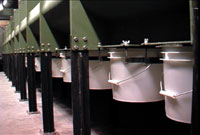 Buckets hanging under a green structure, supported by black metal legs in an industrial setting.