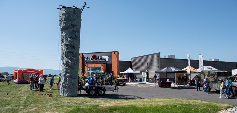Rock climbing wall on grass; people gathered around. Building labeled 