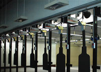 Targets hang on rails in an indoor shooting range, with lighting and equipment visible above.