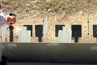 Person aiming a handgun at multiple silhouette targets outdoors.