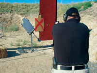 Person shooting at a range; cardboard target with red X nearby.