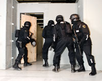 Tactical team training with protective gear entering a reinforced doorway.