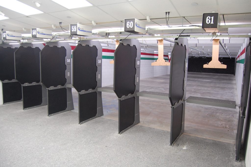 Indoor shooting range with numbered shooting stalls, target carriers, and bullet trap at the far end.