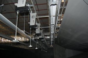 Ceiling-mounted air conditioning ducts with suspended supports in a dimly lit large room.