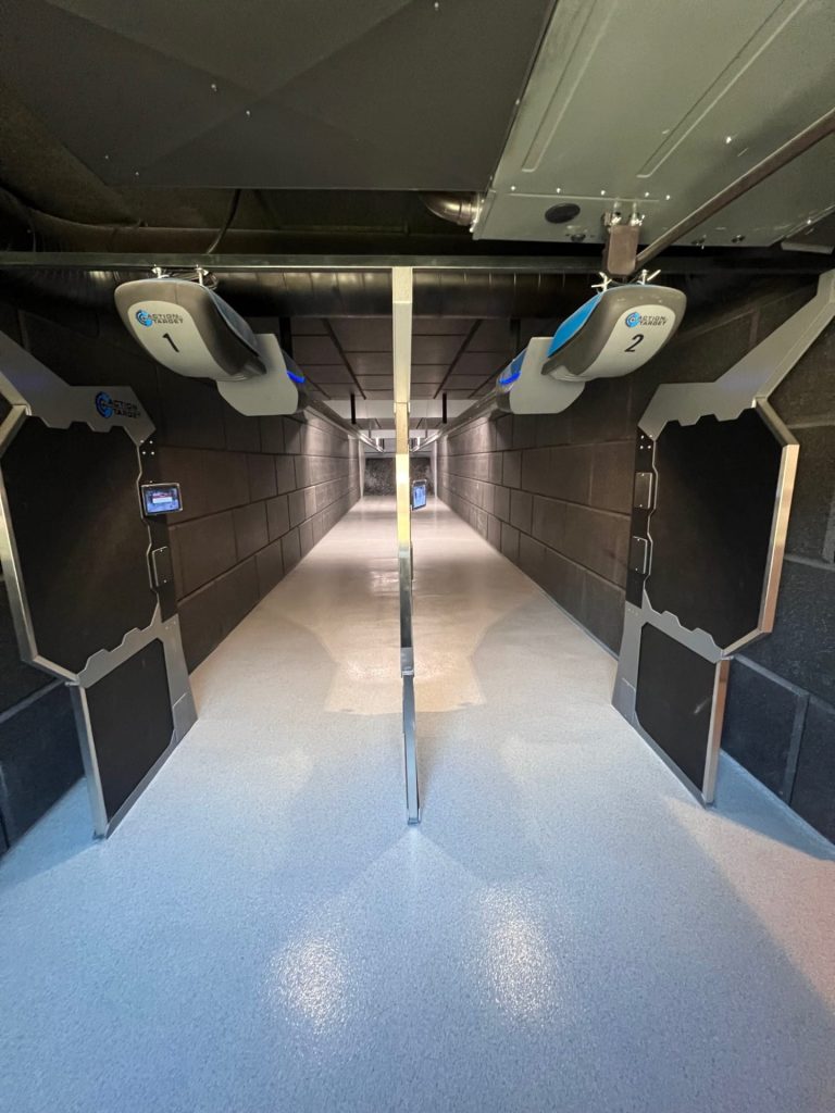 Shooting range lanes with dividers, two overhead numbers, black walls, and a long, narrow corridor.